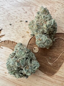 Two cannabis buds on a wooden surface, one on a decorative heart-shaped cut.