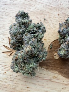Two buds of green cannabis with visible trichomes on a wooden surface.