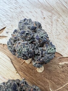 Bud of marijuana with green, purple, and brown colors on a wooden surface.