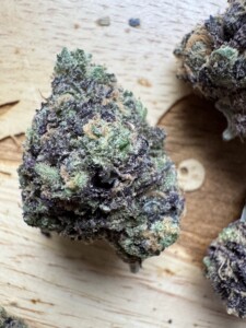 Bud of cannabis, with green, purple, and tan hues, against a wooden surface.