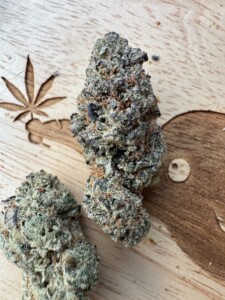Two cannabis buds on a wooden surface with a carved marijuana leaf.