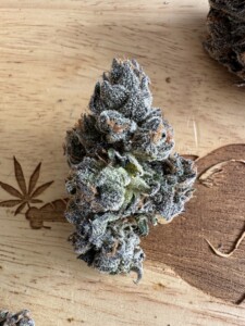 Bud of cannabis covered in trichomes on a wood surface with a cannabis leaf carving.