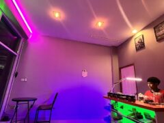 Interior view of a shop with purple and green neon lights and a person behind a counter.