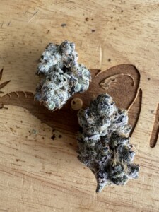 Two cannabis buds on a wooden surface, with brown and green hues.
